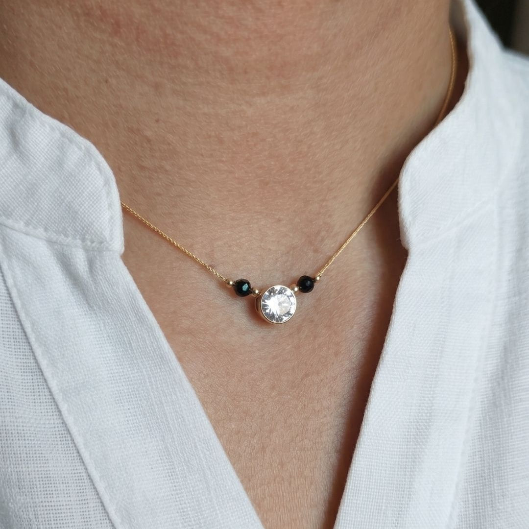 Necklace with a central gemstone and two smaller stones worn by a person in a white shirt.