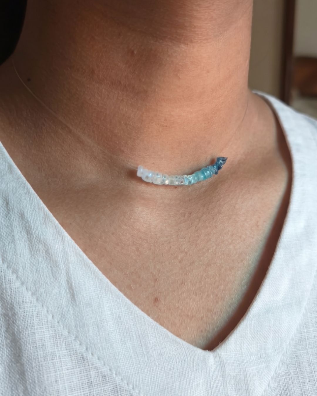 Necklace with a blue gemstone on a person wearing a white shirt.