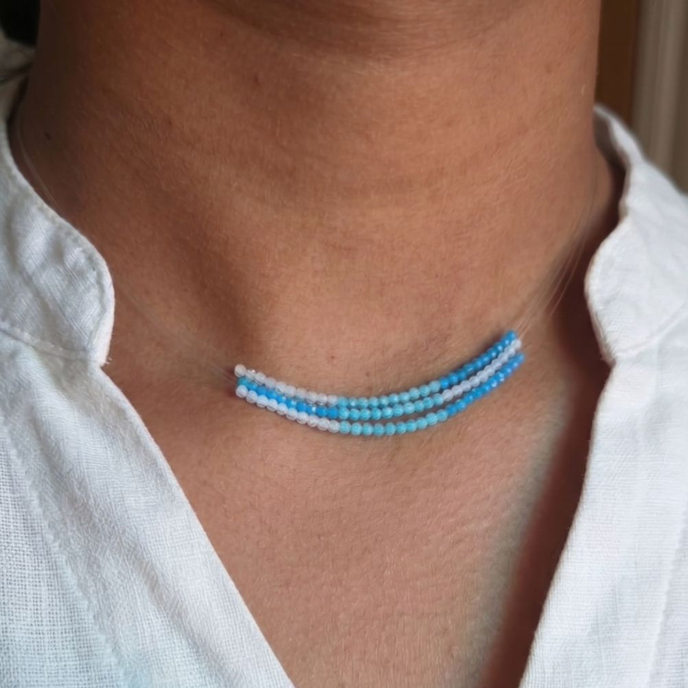 Close-up of a person wearing a blue beaded necklace with a white shirt.
