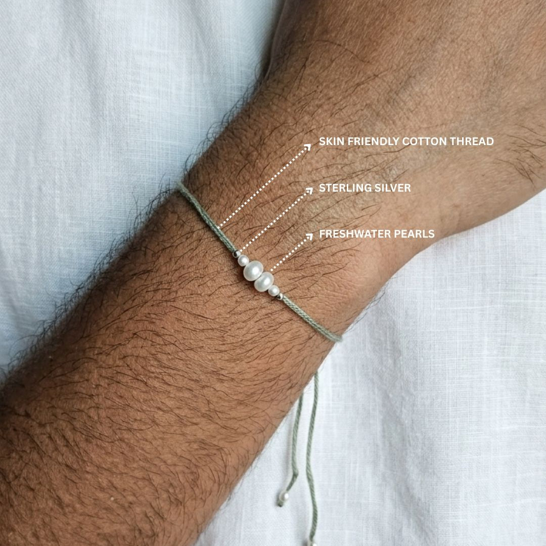 A close-up of a person's wrist wearing a delicate multi-strand bracelet. The bracelet features three thin strands: one made of skin-friendly cotton thread, one of sterling silver beads, and one with three freshwater pearls.