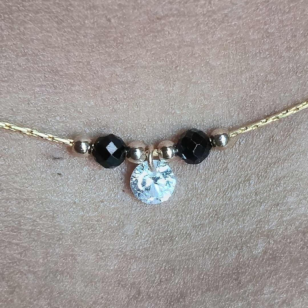 Necklace with black beads and a clear crystal pendant on a beige background