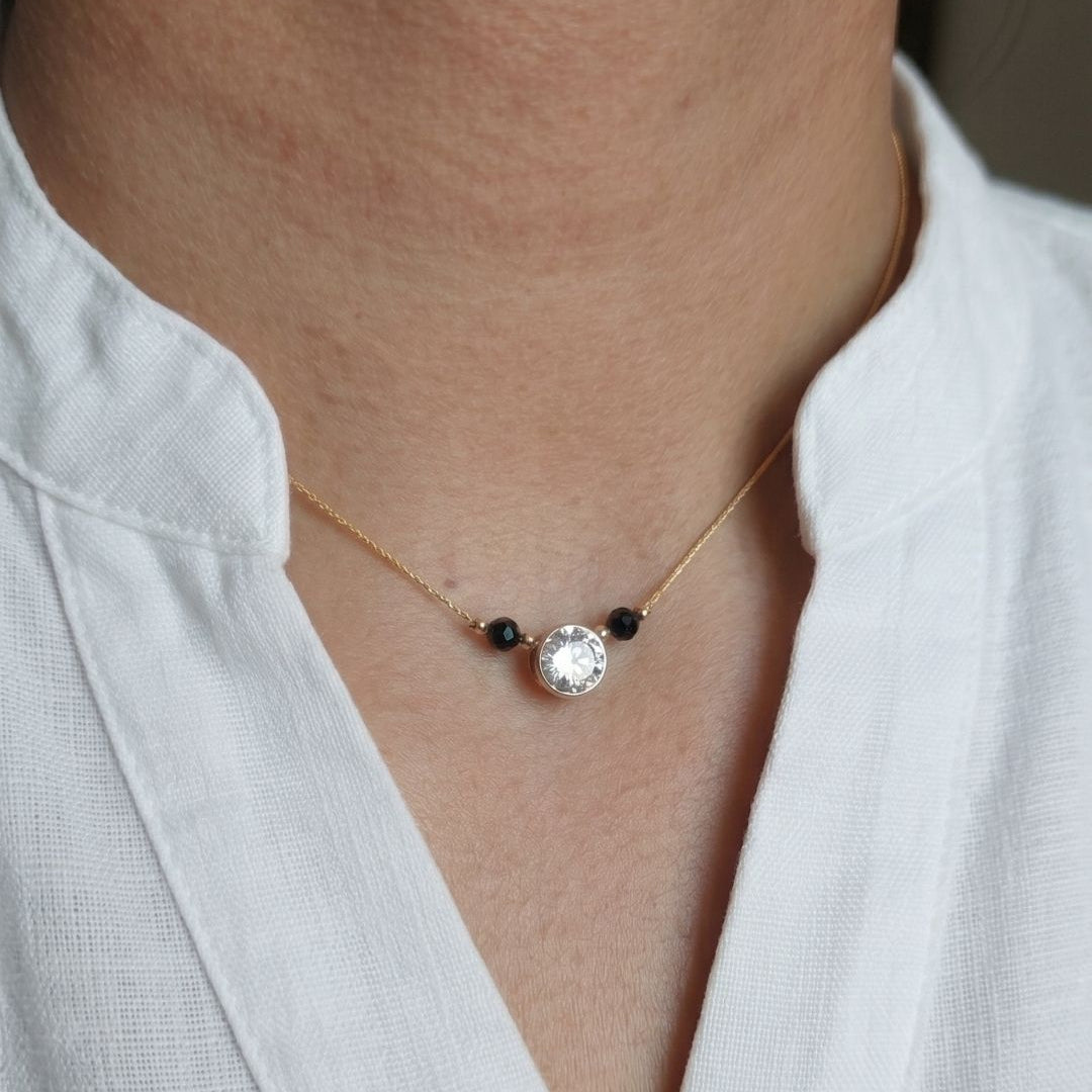 Necklace with a central gemstone and black beads worn by a person in a white shirt.