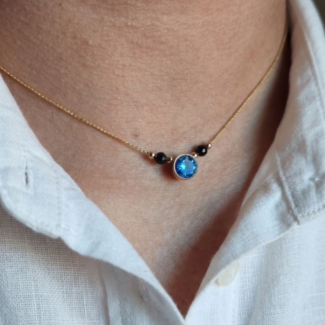 Necklace with a blue gemstone worn by a person in a white shirt