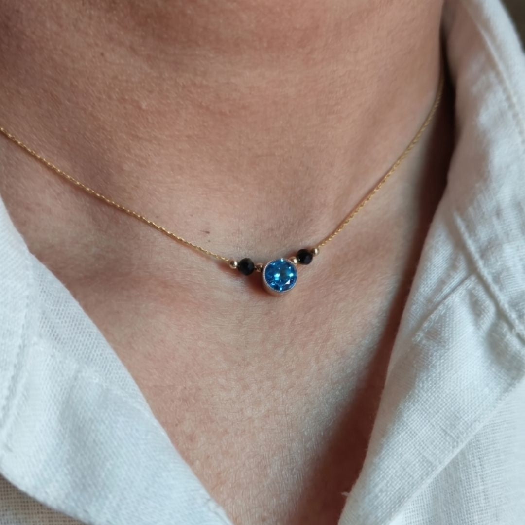 Necklace with a blue gemstone worn by a person in a white shirt