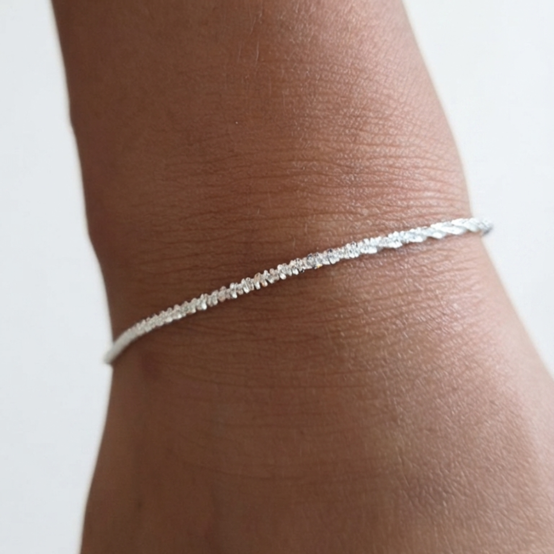 A delicate silver chain bracelet worn on a person's wrist, shown in a close-up shot against a plain light background.