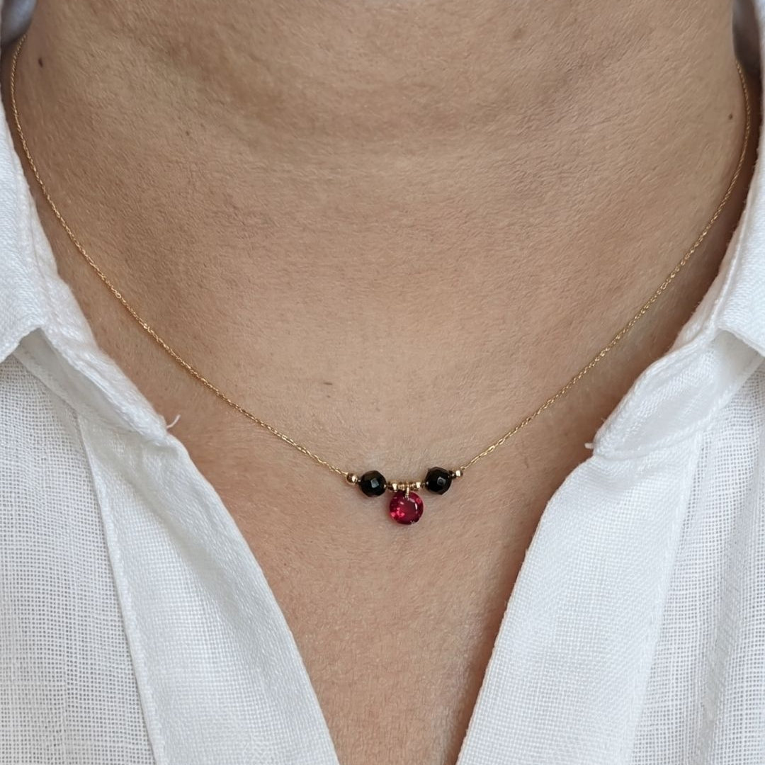 Necklace with red and black gemstones worn by a person in a white shirt