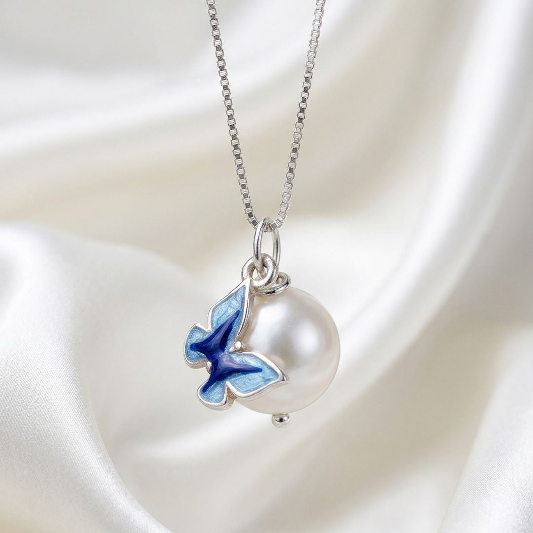 Pearl necklace with a blue butterfly pendant on a satin background, featuring the brand 'MinniM'.