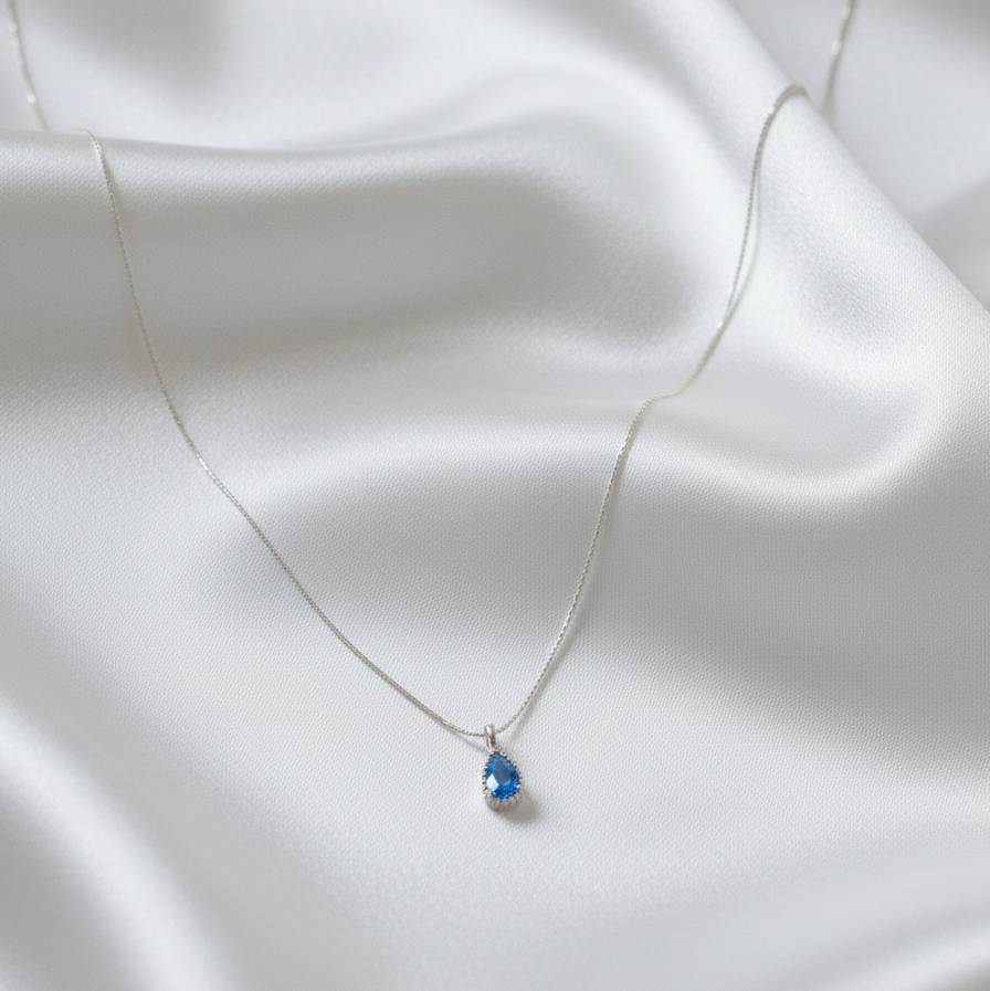 Silver necklace with a blue teardrop pendant on a white fabric background