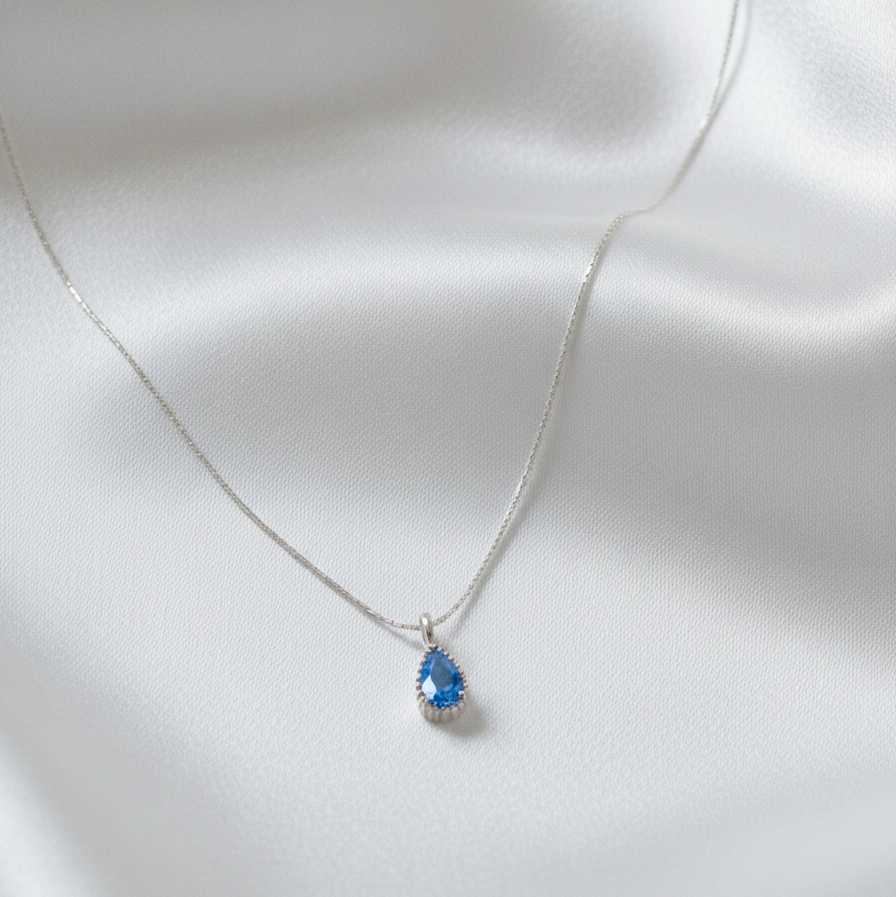 Sterling silver necklace with a blue pendant on a white satin background