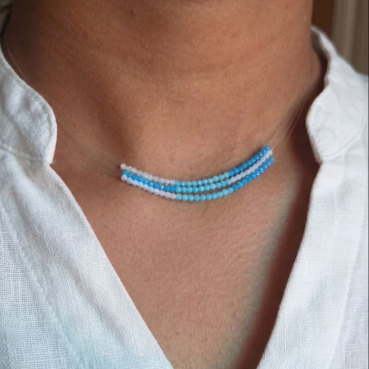 Close-up of a person wearing a blue zircon necklace with a white shirt.
