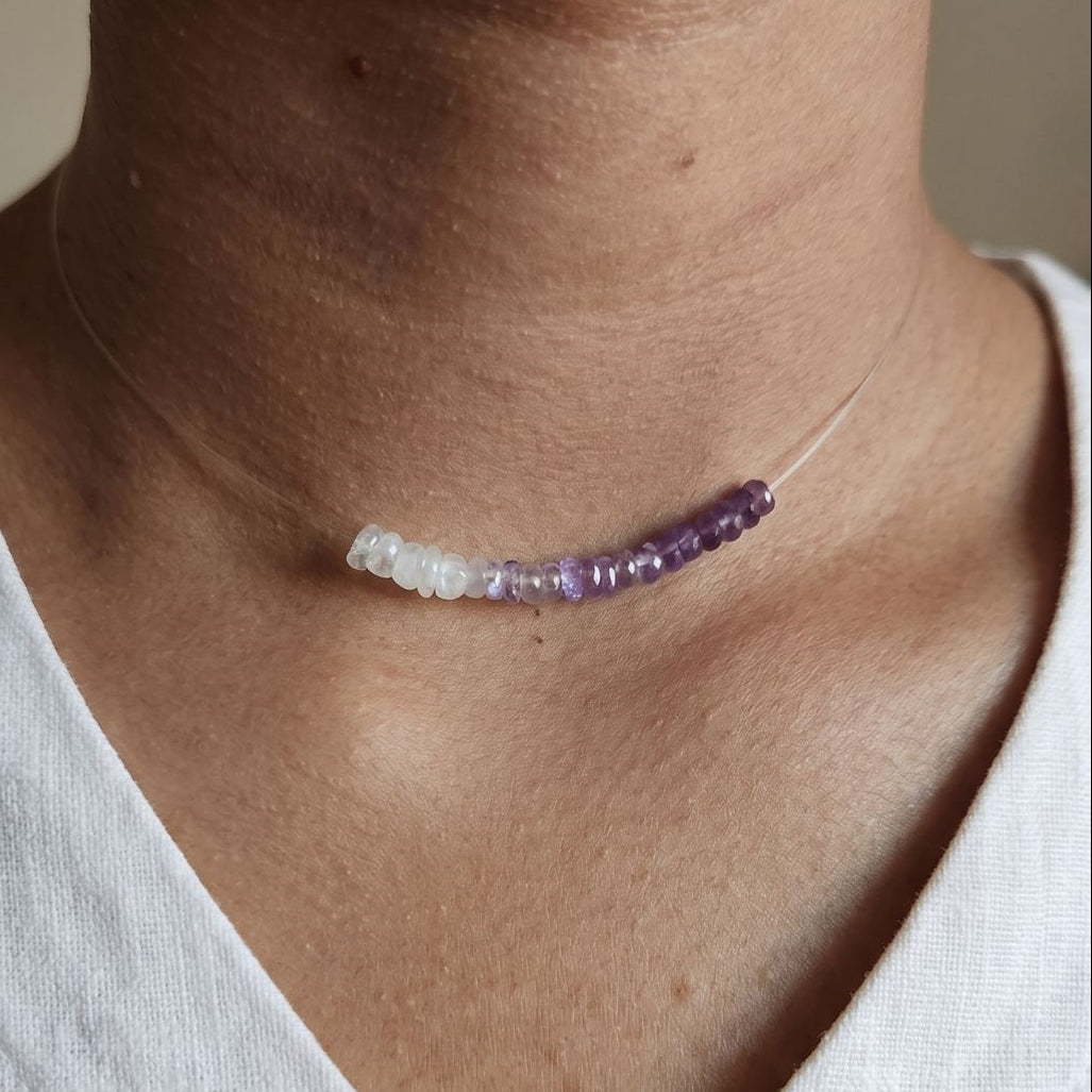 Necklace with purple and white beads worn by a person in a white shirt.