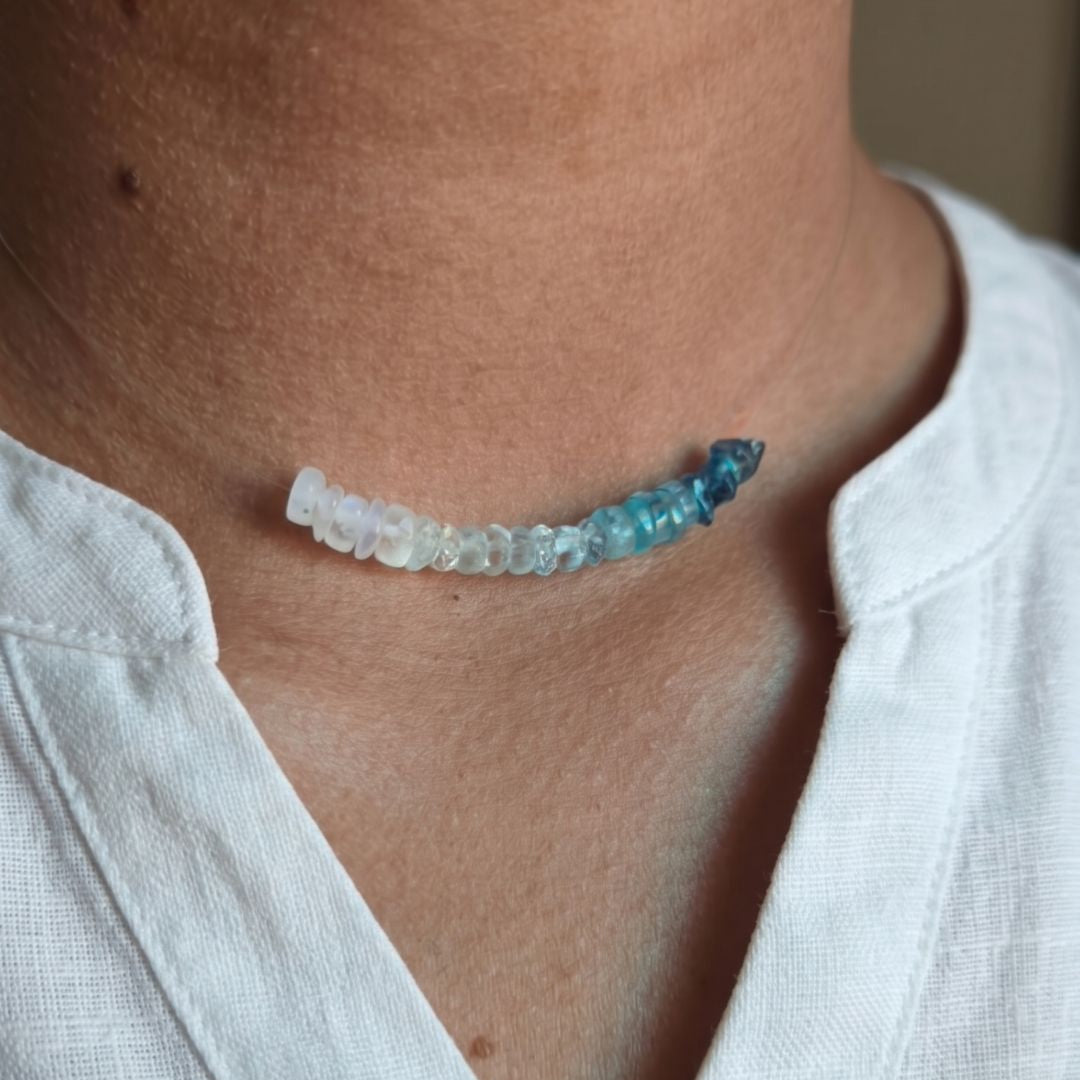 Necklace with blue and clear beads worn by a person in a white shirt.