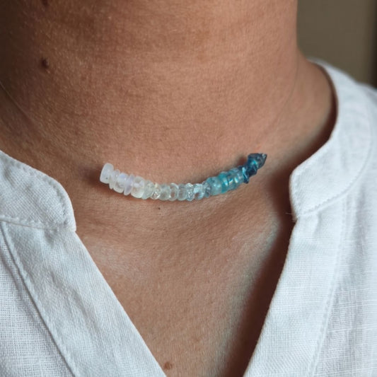 Necklace with blue and clear beads worn by a person in a white shirt.