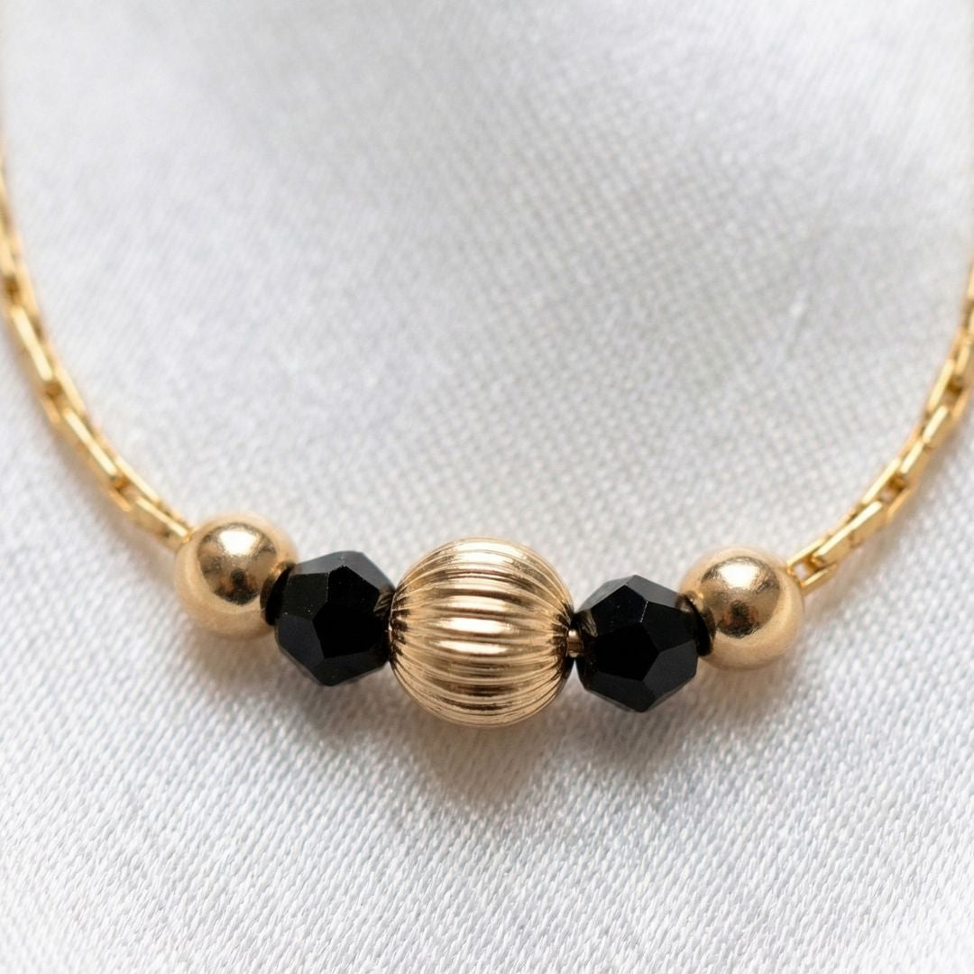 Gold and black beaded bracelet on a white background with 'Minnim' branding.