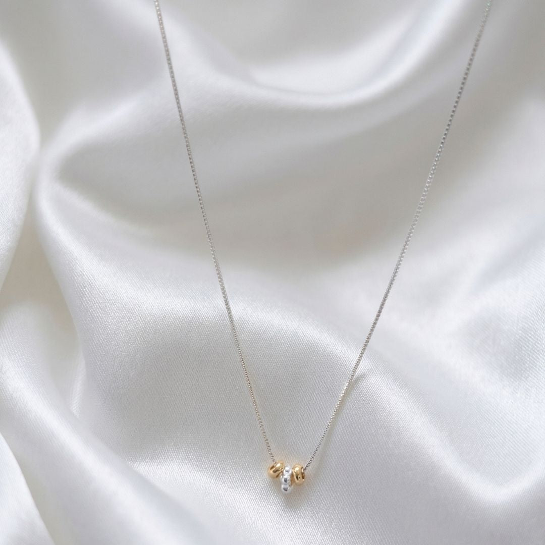 Necklace with a small round pendant on a white fabric background, branded 'MinniM'.