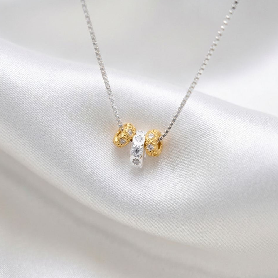 Necklace with a gold and silver pendant on a white satin background, featuring the brand 'MinniM'.