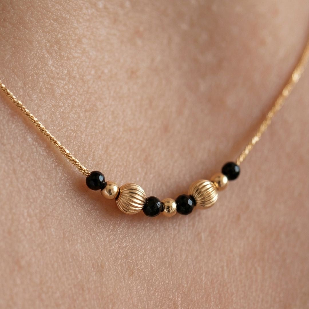 Necklace with gold and black beads on a skin background, featuring the brand 'MinniM'.