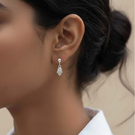 Close-up of a woman wearing a silver hamsa hand earring against a neutral background