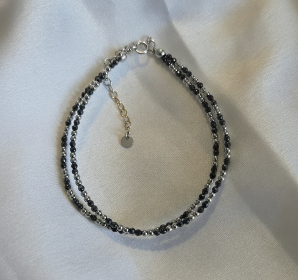 Beaded bracelet with black and silver beads on a white fabric background