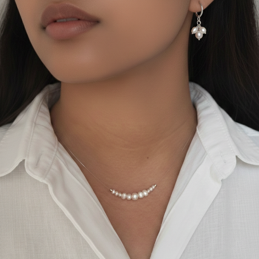 Close-up of a person wearing a pearl necklace and earrings with a white shirt.